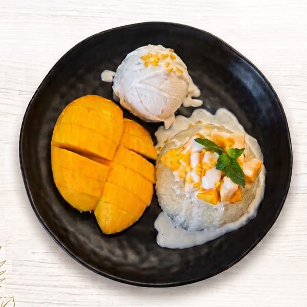 Mango sticky rice with coconut ice cream, topped with mint, on a black plate.