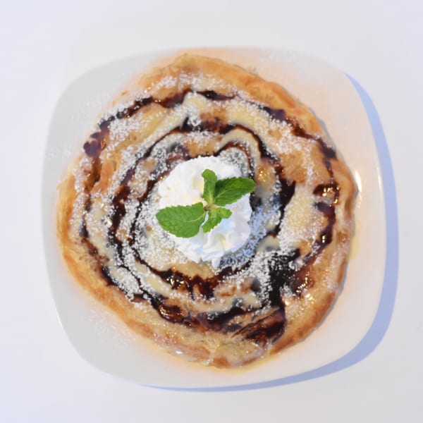 Golden roti pancake drizzled with chocolate sauce, condensed milk, powdered sugar, whipped cream, and mint.