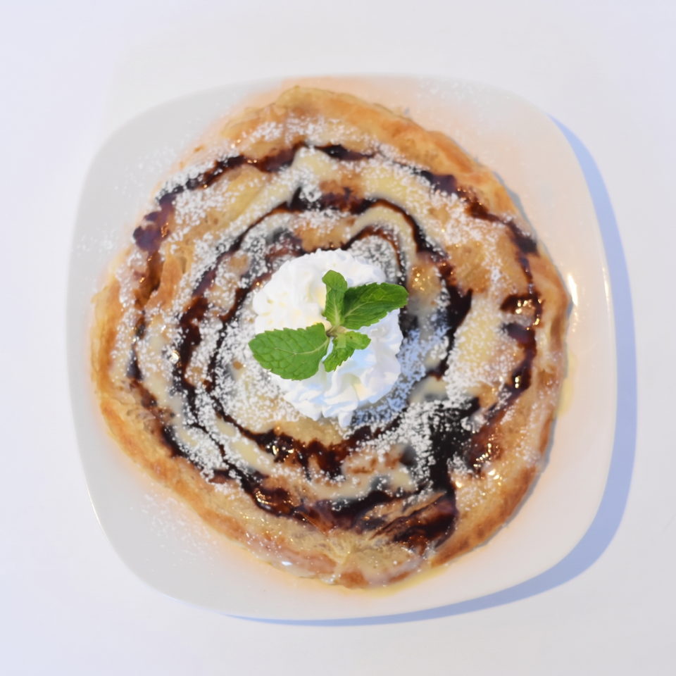 Golden roti pancake drizzled with chocolate sauce, condensed milk, powdered sugar, whipped cream, and mint.