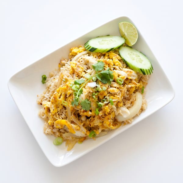 Crab fried rice with scrambled egg, cilantro, green onions, cucumber slices, and a lime wedge.