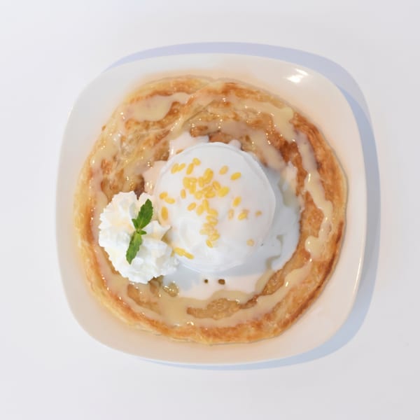 Roti with a scoop of coconut ice cream, mung beans, whipped cream, and mint on a white plate.