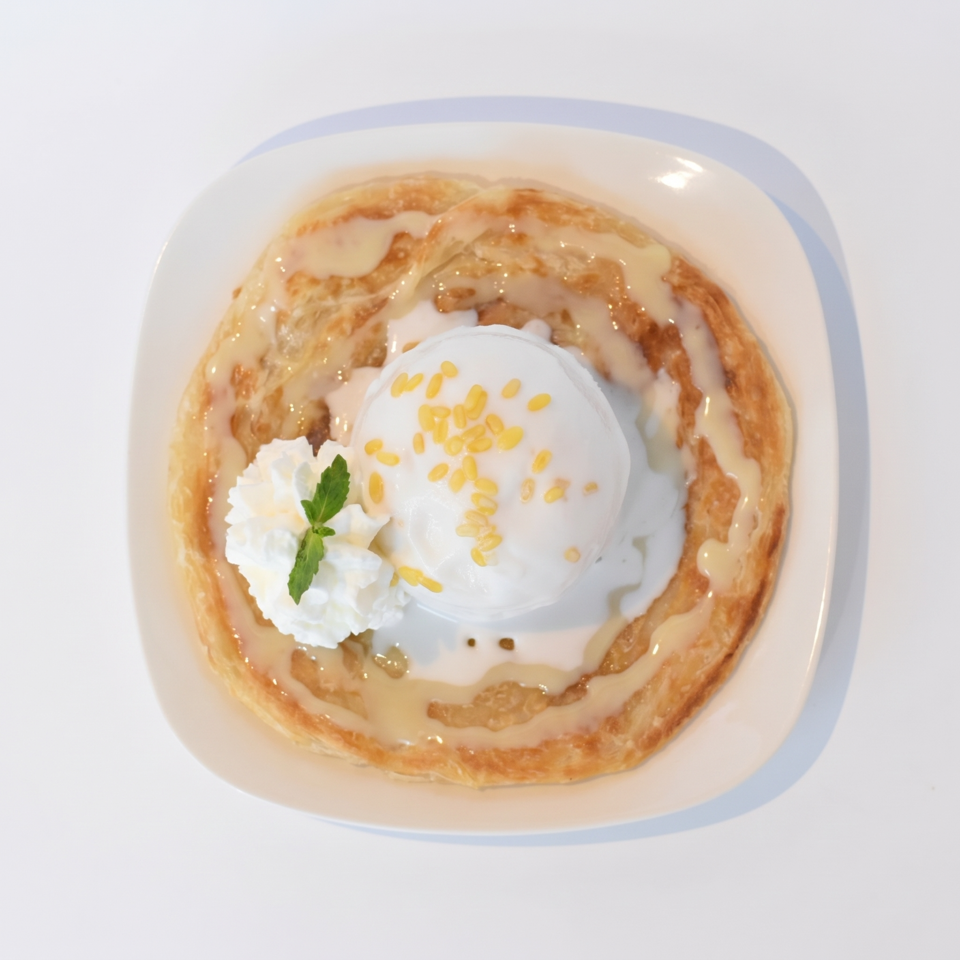 Roti with a scoop of coconut ice cream, mung beans, whipped cream, and mint on a white plate.