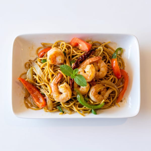 Shrimp lo mein with red and green bell peppers, onions, and mint garnish on a white plate.