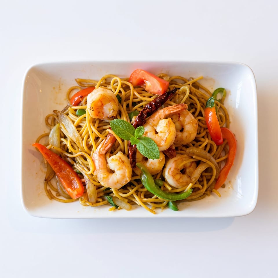 Shrimp lo mein with red and green bell peppers, onions, and mint garnish on a white plate.