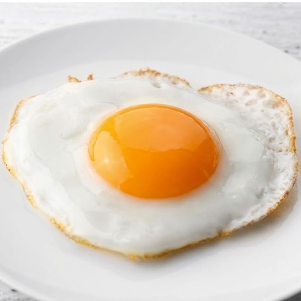 Sunny-side-up fried egg with a bright golden yolk served on a white plate.