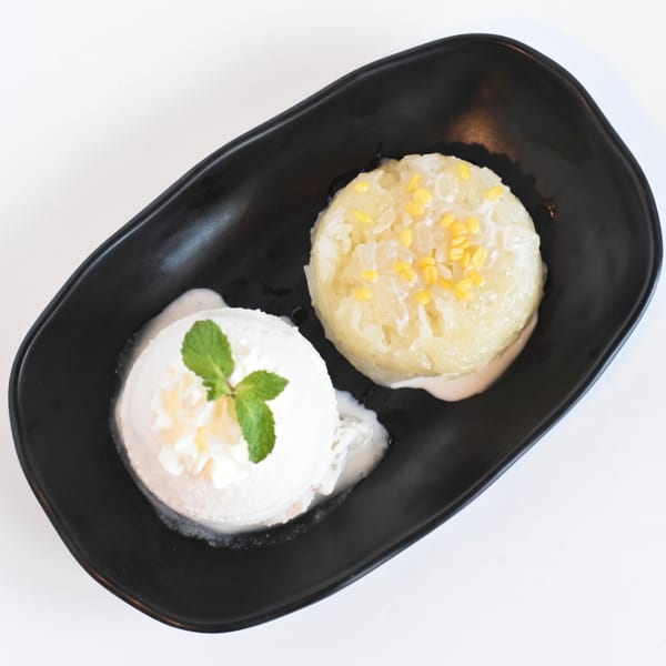A black plate holds a scoop of vanilla ice cream with mint and a mound of sticky rice.